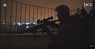 A sniper with a mask and an M24 rifle next to him in the field