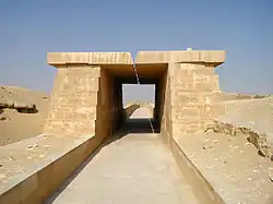 A paved way of white limestone covered with a roof made of massive stone blocks resting on equally massive walls.