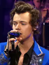 A man with brown hair singing behind a microphone wearing an electric blue suit with sparkly lapels and cuffs