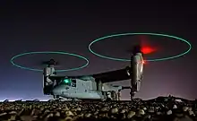 Ground crew refuels an MV-22 before a mission in central Iraq at night. The rotors are turning and the tips are green, forming green circles.