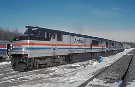A gray diesel locomotive with a black roof. On the side are red, white, and blue stripes of equal width.