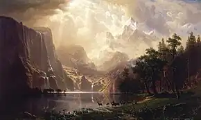Painting of a lake with deer at the water's edge and the Sierra Nevada in the background. Light is shining between the clouds onto the mountains.