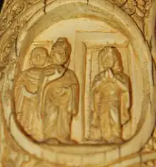 Ivory tusk with three figures: the Buddha, another attending monk, and a female figure standing in a doorway.