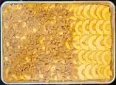 Rectangular baking sheet, with rows of raw apple slices on top of cake batter.  Two-thirds of the apples are covered by cinnamon-scented streusel