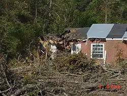 A brick home with part of its roof collapsed due to fallen trees.