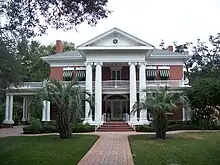 an old southern neoclassical-styled mansion with manicured lawn and palm trees