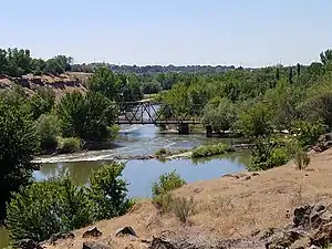 A river flows under a steel bridge through a wooded area