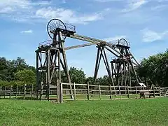 Twin timber frames of winding gear topped with spoked metal wheels used to hoist men and coal from underground on a sunny day