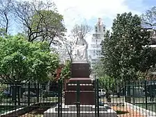 A statue in a plaza, with trees at the sides, and wires around it.