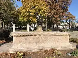 A large, rectangular, pink granite base with a smaller, aged bronze statue of a boy and turtle sitting in the center of the base.