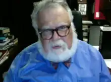 Celal Şengör is a white caucasian male, he has white hair and beard and he has glasses.