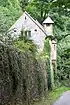 Beyond a tall wall is the end of a chapel with a triple window in the gable, a shorted tower to the right with a pyramidal roof, and an oriel window protruding more to the right