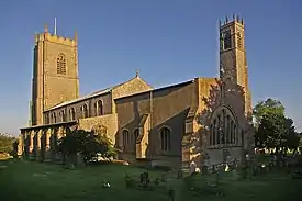 View of the church bathed in early morning sunlight. There is a large tower at the further end, and a small tower beside the chancel.
