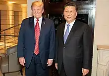 Donald Trump and Xi Jinping stand next to each other, both smiling and wearing suits