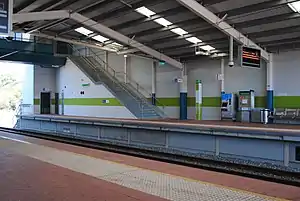 Station platforms with shelter covering the platforms and tracks and stairs heading up to a foodbridge