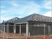 A hip roof construction in Northern Australia showing multinail truss construction. The blue pieces are roll formed metal roof battens or purlins. This roof is built with purpose-made steel hook bracket which is bolted to the truss with M16 bolt. The bracket is bolted to an M16 bolt cast in situ, embedded 300&nbsp;mm (12&nbsp;in) into the reinforced concrete block wall.  This system is typically in place every 900&nbsp;mm (35&nbsp;in) around perimeter