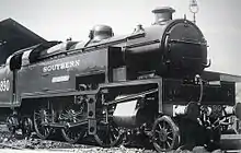 Side-and-front view of the 3-cylinder version of the locomotive. The distinguishing feature is a full-width flat panel rising vertically above the front buffer beam to the level of the bottom of the smokebox door. The water tanks are a different shape from the K Class, as they include a rectangular access hole in the side, bottom-front, for maintaining the valve gear, which is also different from the K class.