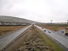 A four-lane freeway with a wide median approaching a residential neighborhood with an overpass in the distance.