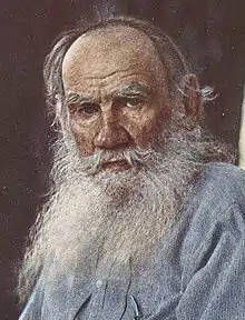 Man with long white, whispy beard wearing a blue button-down shirt