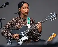 A black woman wearing a leopard print shirt performs with a guitar