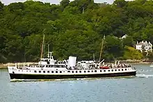 Broadside view of ship, with black hull and white superstructure, steaming right to left