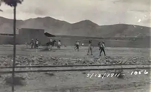A group of men wearing sombreros walking along a dirt road between a railroad track and a line of buildings. Dated 5/13/1911.