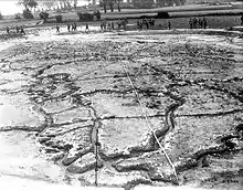 a vast full-scale model of the Vimy Ridge battlefield sprawls out across the landscape, resembling a football field in size. The intricate details of the terrain, including trenches, craters, and rough terrain, are meticulously recreated, providing a vivid representation of the historic battleground. Along the periphery of the model, soldiers stand, their figures adding a human dimension to the scene. The soldiers' presence serves to contextualize the scale of the battlefield model.