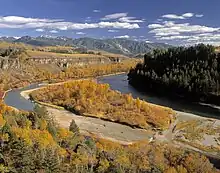 A river flows through a mountain valley lined with autumn foliage