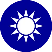 A blue circular emblem on which sits a white sun composed of a circle surrounded by 12 rays.