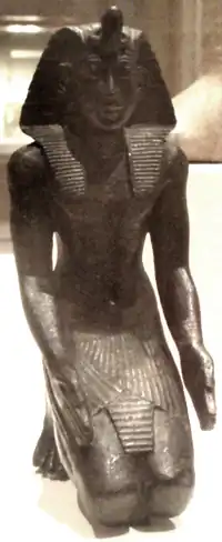 A small kneeling bronze statuette, likely Necho II, now residing in the Brooklyn Museum