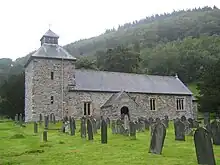 View of the church from the churchyard: a stone church with a square tower and a small porch, surrounded by old gravestones.