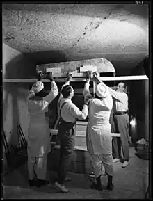 Four men lifting large wooden beams that support a decorated lid