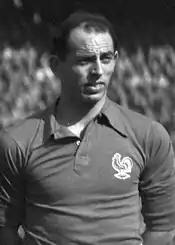 A black and white photography of a light-skinned man wearing a shirt with a rooster on the left chest.
