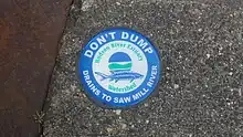 A blue and green circular medallion on a sewer warning that the discharge goes into the river