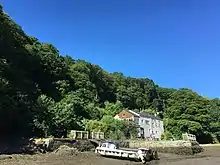 A building with a dock area for boats, surrounding by trees and dried-up river bed