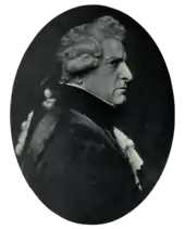 Right profile of stern-faced man in dark clothing with lacy shirt and cuffs, wearing a wig