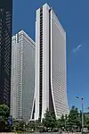 Ground-level view of a thin, brown and white high-rise; the two wider sides curve and flair out as they near the bottom
