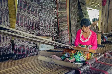 T'boli dream weavers using two-bar bamboo backstrap looms (legogong) to weave t'nalak cloth from abacá fiber. One bar is attached to the ceiling of the traditional T'boli longhouse, while the other is attached to the lower back. Philippines.