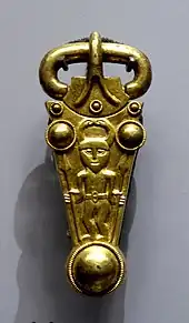 A gold buckle decorated with a man in a horned helmet carrying a spear in each hand.