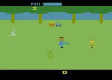 A video game sprite representing Leatherface, facing a sprite representing a possible victim. Below Leatherface is a sprite of a bush, to the left of the screen is a sprite of a cow skull. The background is lined with four trees, and distant house and car sprites.
