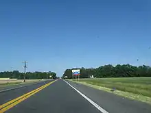 A two-lane road passing through farm fields. A blue and white sign on the right indicates an ongoing construction project on US 113.