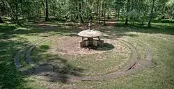 A a concrete model of a flying saucer in a clearing. There are concrete paths beneath and around the model.
