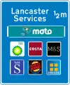 Approach sign to motorway service area listing operator and six franchises available at the stop. These are the only signs allowed to display brand logos.
