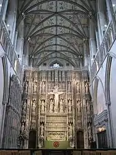 The photo shows the altar of St. Alban's Cathedral, behind which rises a large stone screen with tiers of statues, and a crucifix, centrally placed.