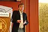 A man talking and gesturing while holding a projector remote
